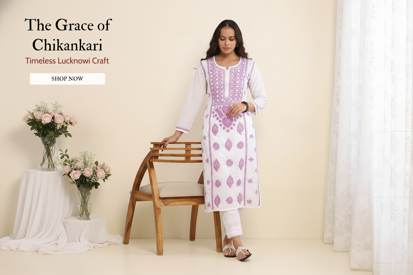 Woman in a white and purple embroidered kurta standing next to a wooden chair with flowers on a table in the background.