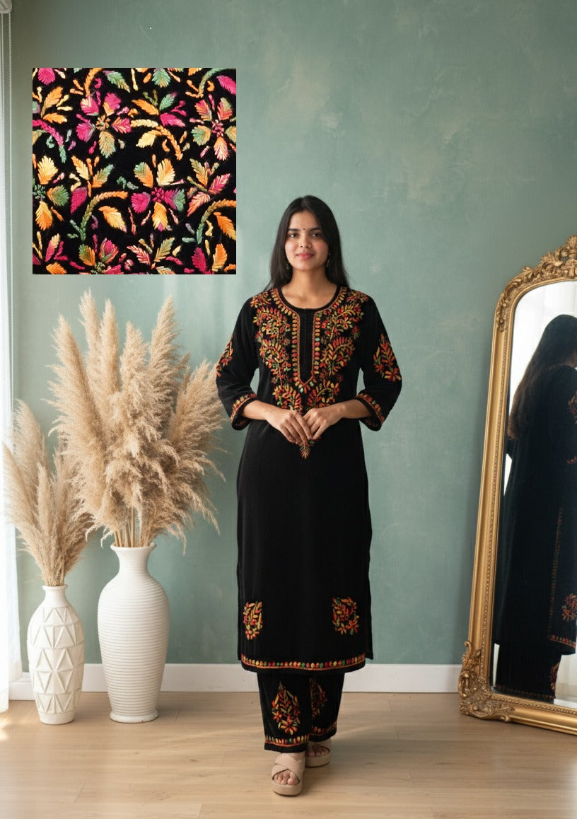 Woman in a black embroidered outfit standing next to a wall with decorative elements.