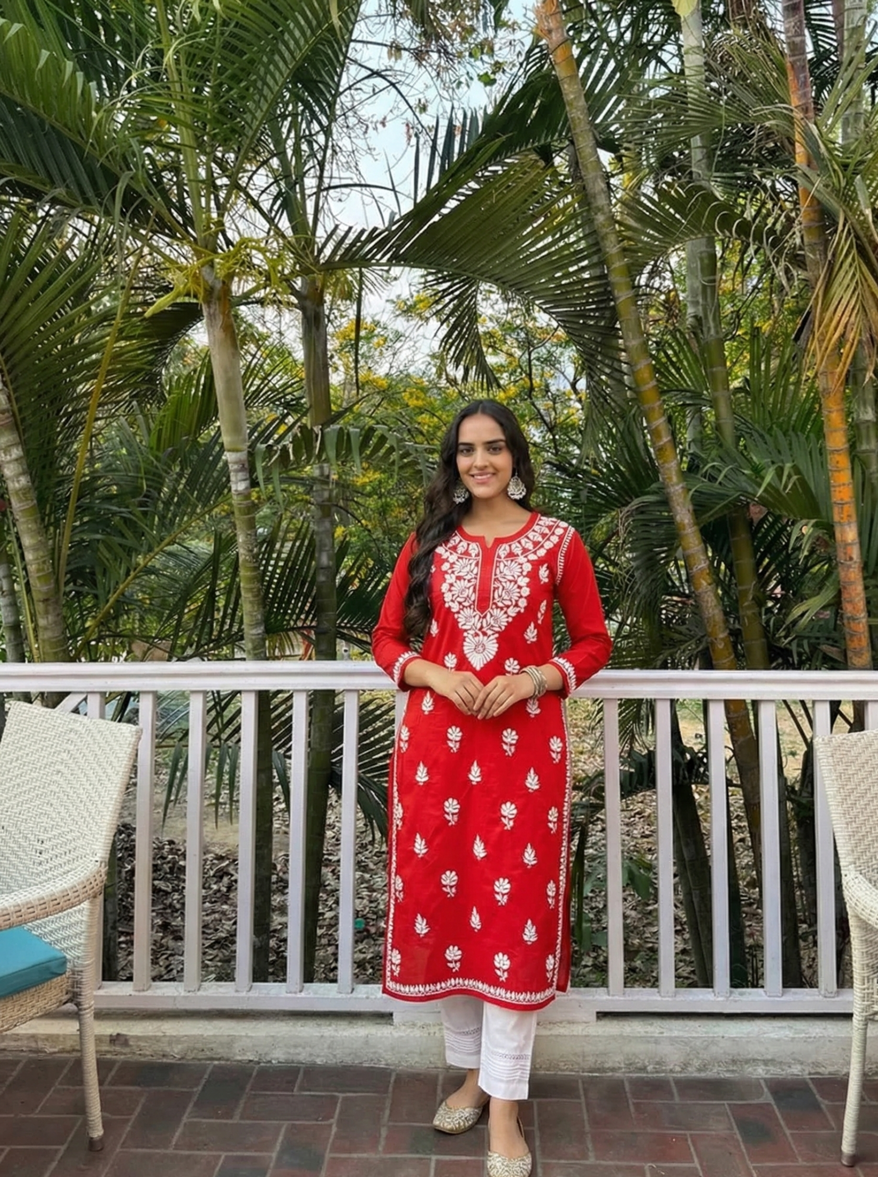 Woman in a red embroidered kurta standing on a balcony with greenery in the background